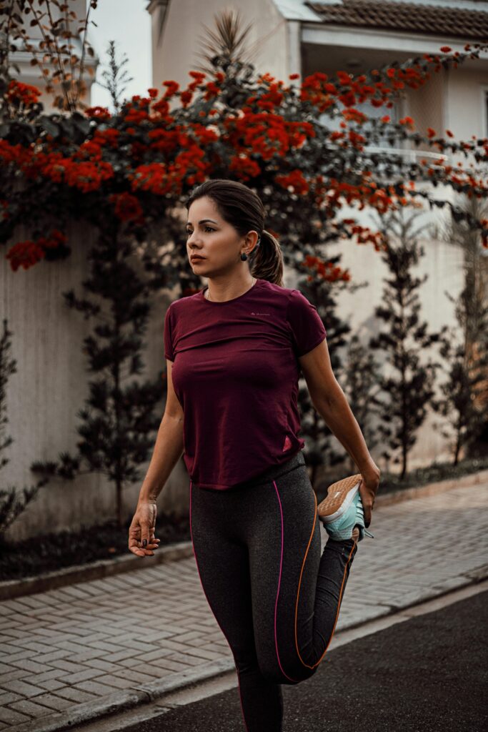 A woman stretches before a run on an outdoor pathway, surrounded by vibrant flowers.