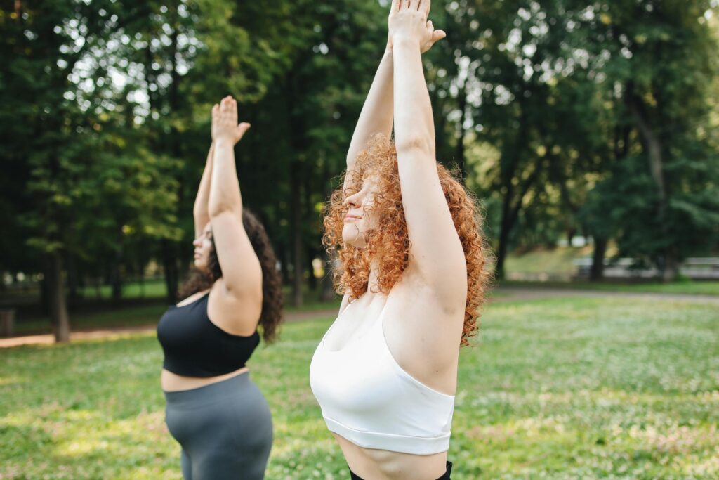 Two women enjoying a yoga session in a lush green park, embracing a healthy lifestyle.